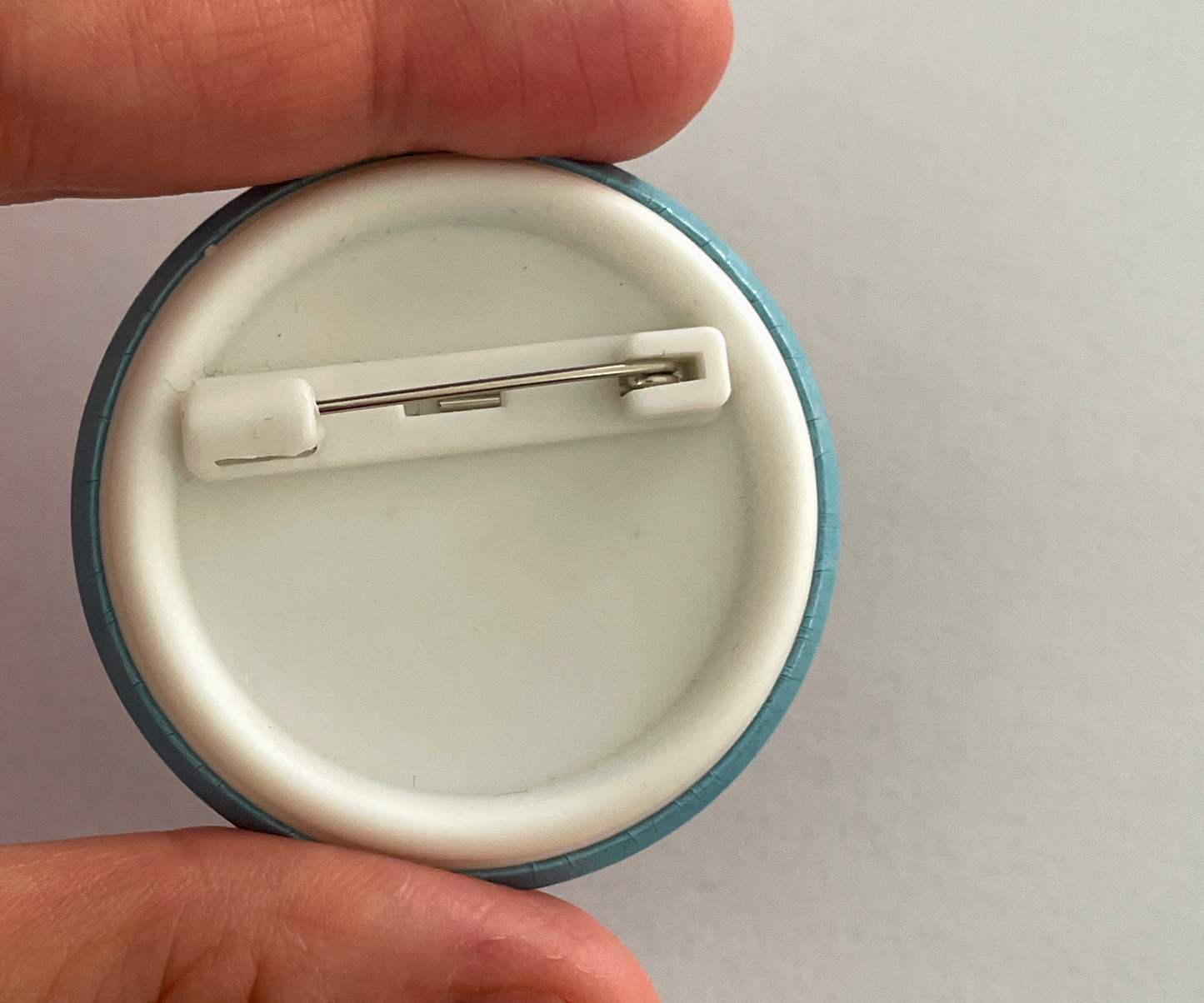 Round button with a pin back held between fingers 